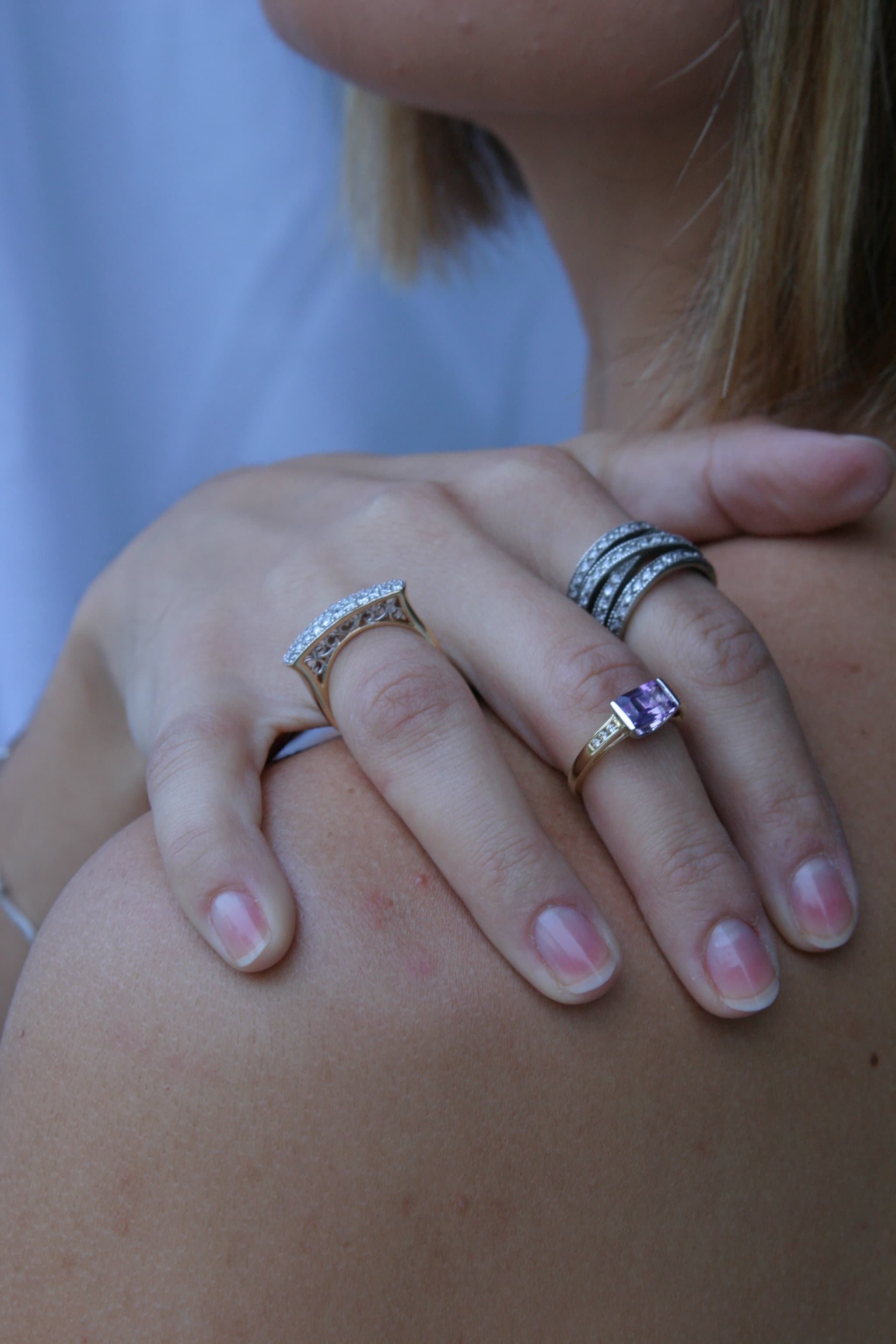 A hand wearing three hand-set rings, one with a purple stone, made at Amber's Jewel Box